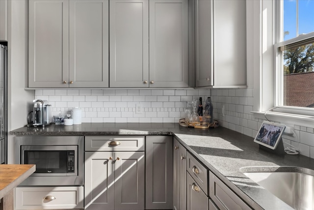 kitchen with dark stone counters, gray cabinetry, stainless steel microwave, and backsplash