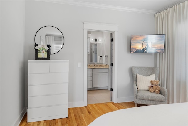 bedroom featuring light wood-type flooring, ensuite bath, sink, and crown molding