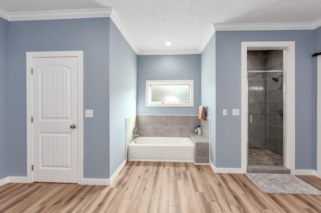 bathroom with a stall shower, a textured ceiling, wood finished floors, baseboards, and a bath