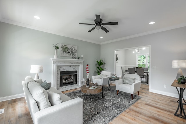 living room with a high end fireplace, ornamental molding, hardwood / wood-style flooring, and ceiling fan