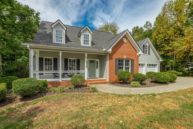 new england style home featuring a porch, a front yard, and a garage