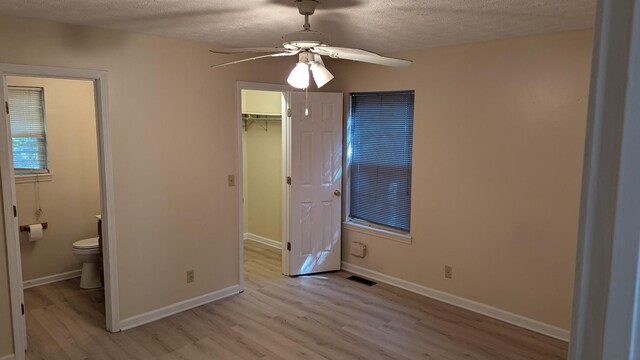 unfurnished bedroom featuring light wood-type flooring, a closet, a spacious closet, ceiling fan, and a textured ceiling