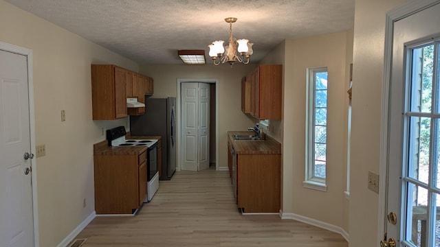 kitchen with brown cabinets, a notable chandelier, electric stove, a sink, and under cabinet range hood