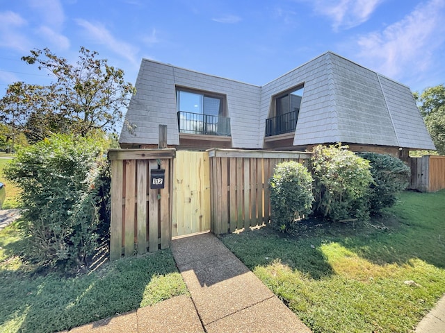 view of front of home featuring a front lawn, a gate, mansard roof, and fence