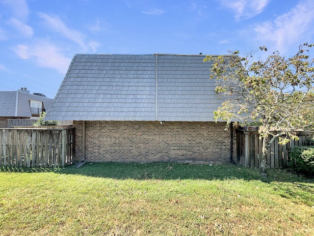 view of side of home with mansard roof, a lawn, brick siding, and fence