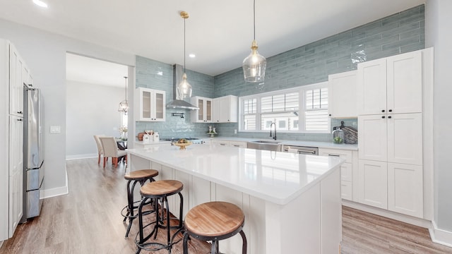 kitchen with a kitchen breakfast bar, decorative light fixtures, wall chimney range hood, and white cabinetry