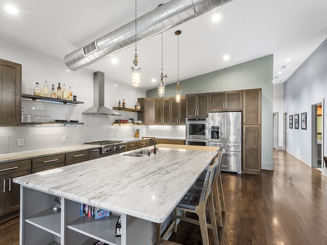 kitchen featuring sink, appliances with stainless steel finishes, wall chimney exhaust hood, and a kitchen island with sink