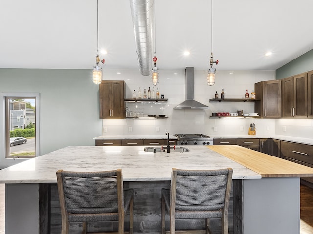 kitchen featuring a breakfast bar area, tasteful backsplash, an island with sink, sink, and wall chimney range hood