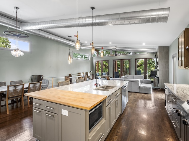 kitchen with dark hardwood / wood-style floors, butcher block countertops, a kitchen island with sink, gray cabinets, and stainless steel microwave