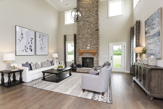 living room with a stone fireplace, crown molding, a high ceiling, an inviting chandelier, and dark hardwood / wood-style flooring