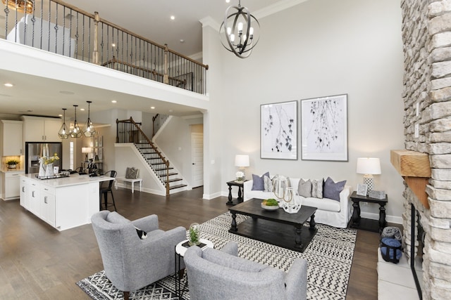 living room featuring a towering ceiling, a fireplace, dark hardwood / wood-style floors, ornamental molding, and a chandelier