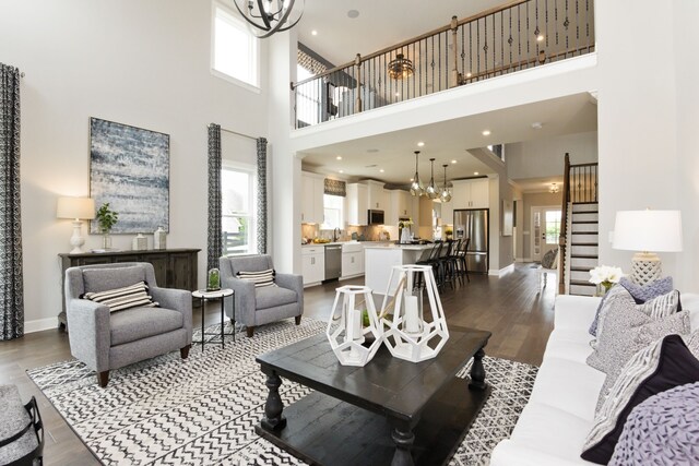 living room featuring dark wood-type flooring, a towering ceiling, a notable chandelier, and plenty of natural light