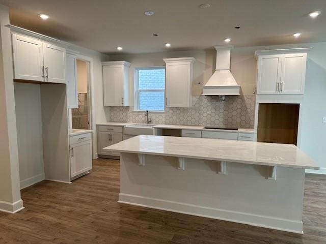 kitchen with white cabinetry, a kitchen island, custom exhaust hood, and sink