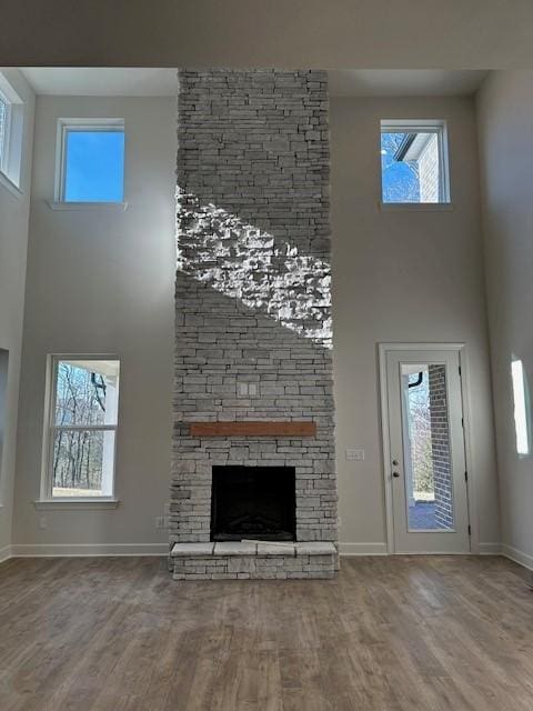 unfurnished living room with hardwood / wood-style floors, a towering ceiling, and a stone fireplace