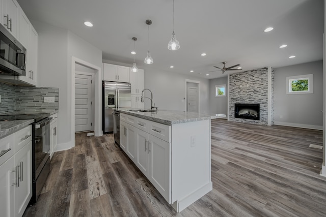 kitchen featuring stainless steel appliances, white cabinetry, sink, a stone fireplace, and ceiling fan