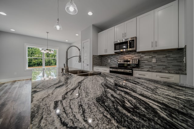 kitchen with pendant lighting, hardwood / wood-style floors, appliances with stainless steel finishes, sink, and light stone counters