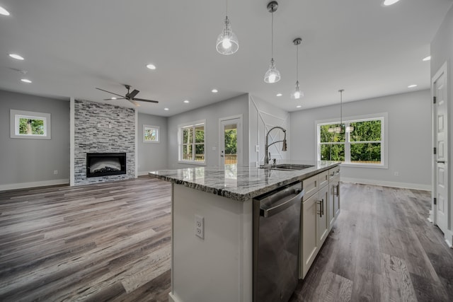 kitchen with a large fireplace, white cabinetry, light stone counters, ceiling fan, and a center island with sink