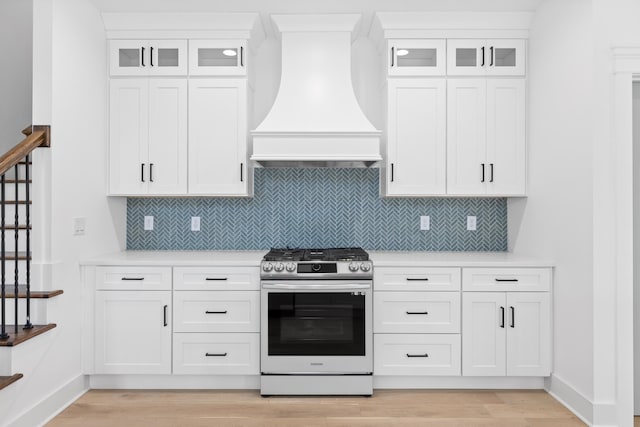 kitchen featuring custom exhaust hood, stainless steel range, light hardwood / wood-style flooring, and white cabinetry