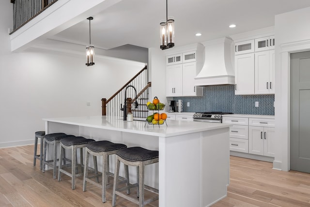 kitchen with custom exhaust hood, hanging light fixtures, a center island with sink, and high end stainless steel range