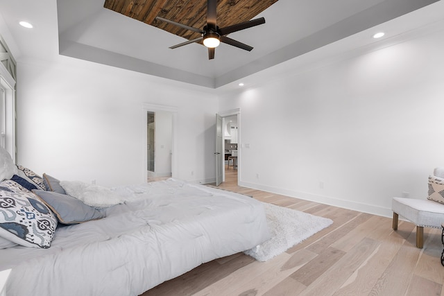 bedroom with ceiling fan, a tray ceiling, and light wood-type flooring