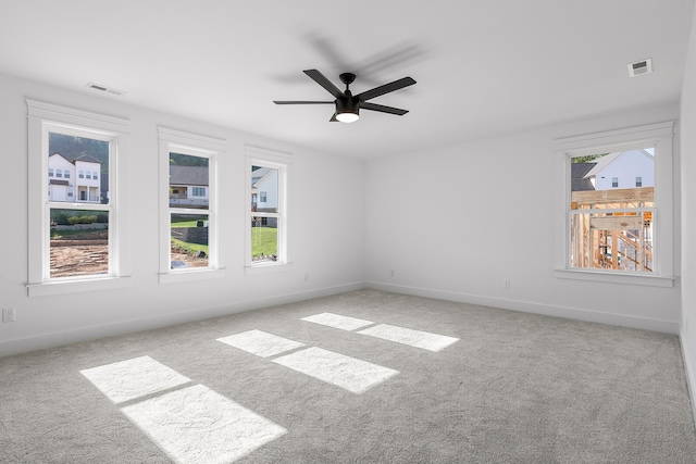 carpeted empty room with ceiling fan and a wealth of natural light