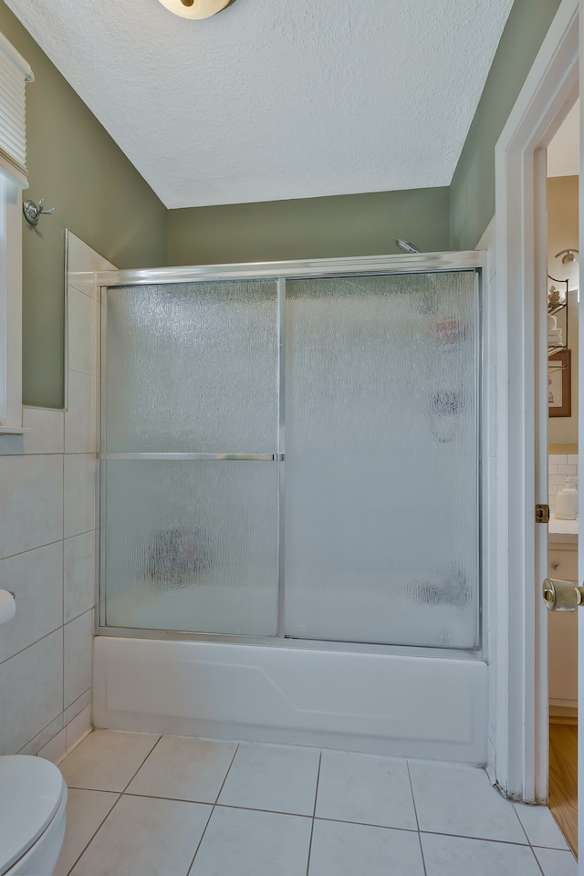 bathroom with a textured ceiling, toilet, tile patterned floors, and enclosed tub / shower combo