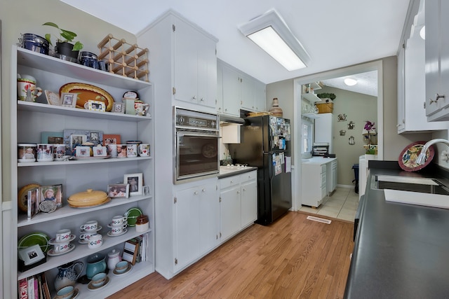 kitchen featuring black appliances, light hardwood / wood-style flooring, sink, washing machine and dryer, and white cabinets