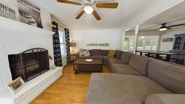 living room with light hardwood / wood-style flooring, ceiling fan, and a brick fireplace