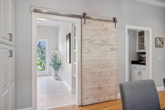 corridor with a barn door, ornamental molding, and light wood-type flooring