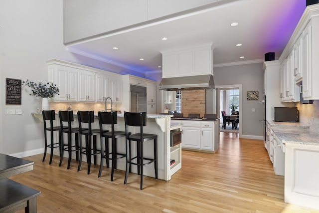 kitchen with a breakfast bar, built in appliances, light stone countertops, light hardwood / wood-style floors, and white cabinetry