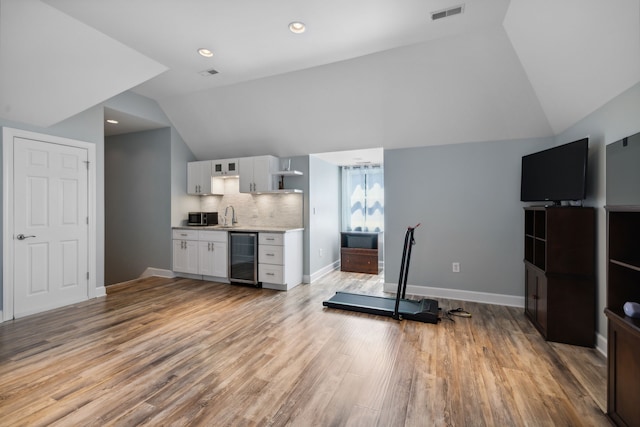 interior space with wine cooler, light hardwood / wood-style floors, vaulted ceiling, and sink