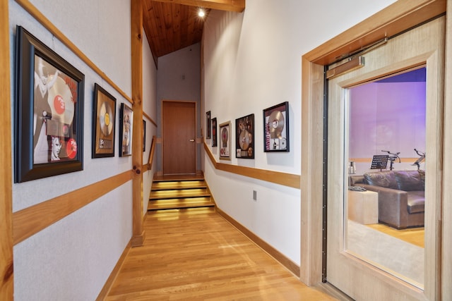 corridor with light wood-type flooring and high vaulted ceiling