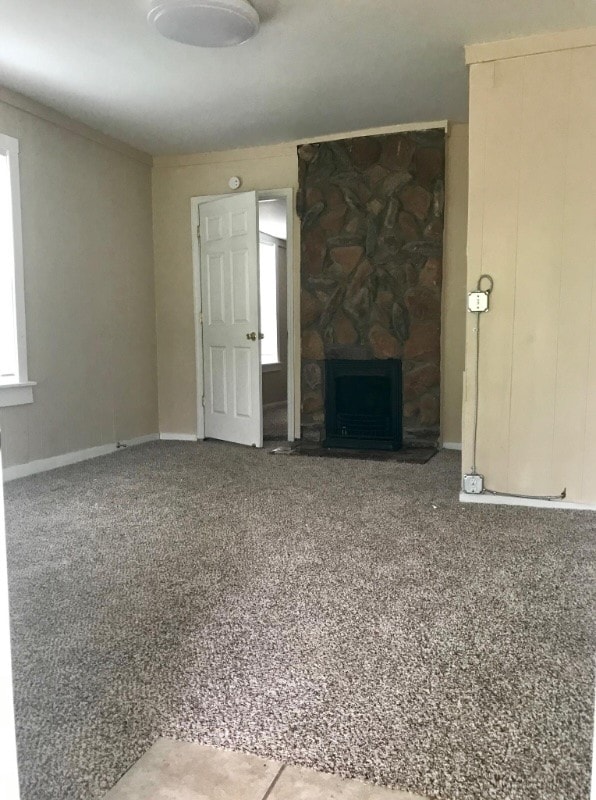 unfurnished living room with carpet flooring and a stone fireplace