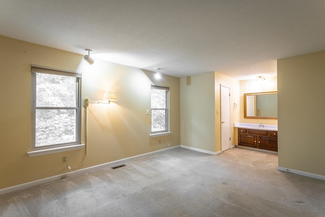 unfurnished bedroom featuring a textured ceiling, connected bathroom, and light colored carpet