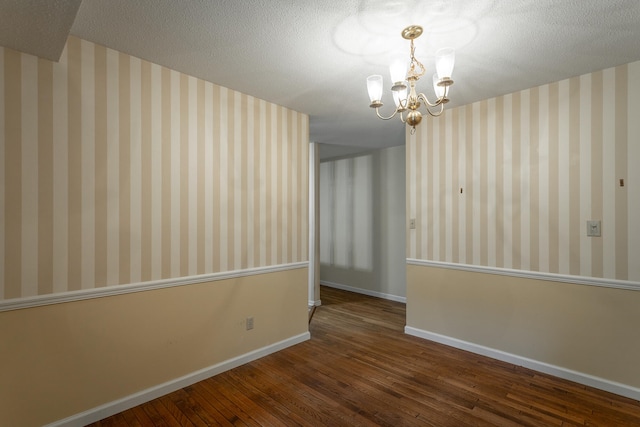 unfurnished room featuring a textured ceiling, dark wood-type flooring, and an inviting chandelier