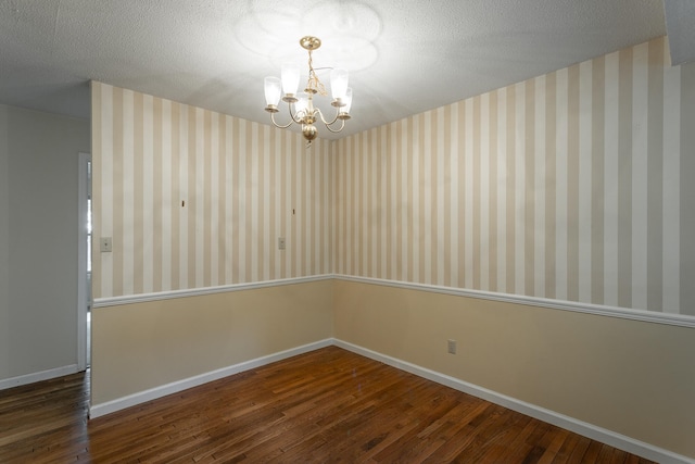 spare room with dark hardwood / wood-style flooring, an inviting chandelier, and a textured ceiling