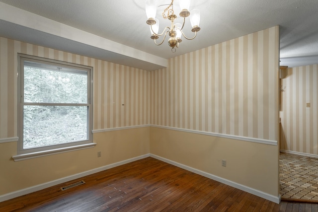 unfurnished room with a wealth of natural light, dark wood-type flooring, a notable chandelier, and a textured ceiling