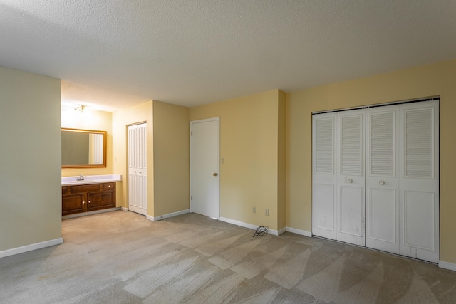 unfurnished bedroom featuring two closets, light colored carpet, ensuite bathroom, and a textured ceiling