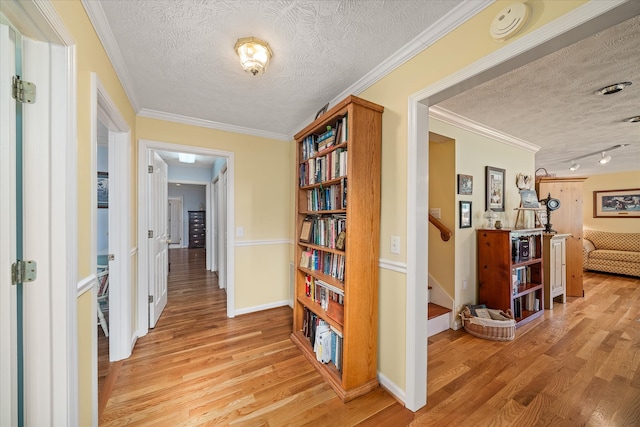 corridor with light hardwood / wood-style floors, a textured ceiling, and crown molding