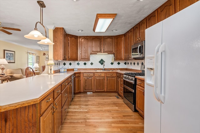 kitchen with ornamental molding, stainless steel appliances, light wood-type flooring, pendant lighting, and kitchen peninsula