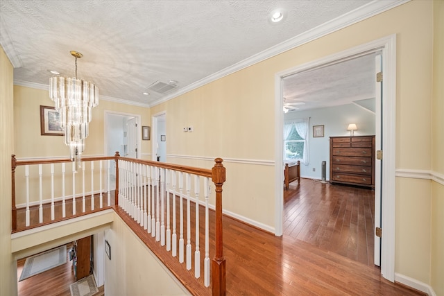 hallway featuring hardwood / wood-style flooring, a chandelier, a textured ceiling, and ornamental molding