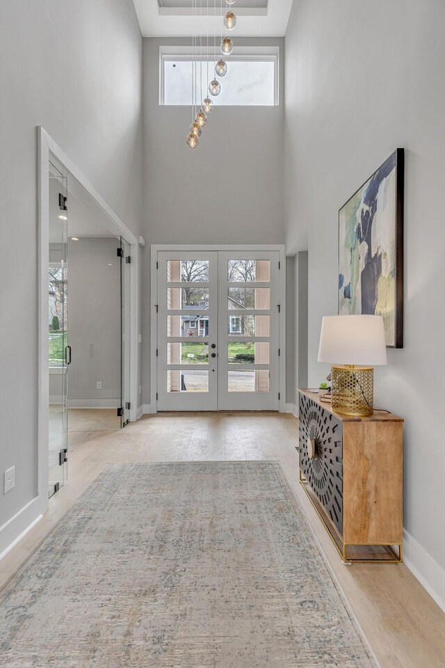 foyer with a high ceiling, a notable chandelier, light wood-type flooring, and french doors