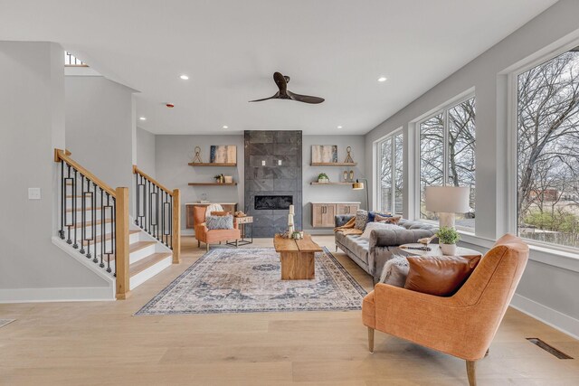 living room with a tiled fireplace, plenty of natural light, ceiling fan, and light hardwood / wood-style floors