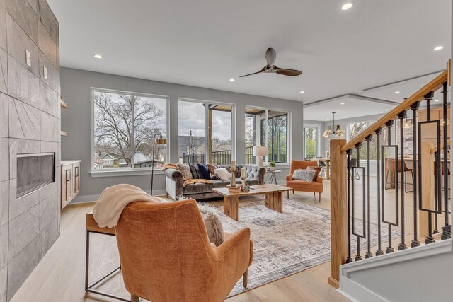 living room with light wood-type flooring, ceiling fan with notable chandelier, and a tiled fireplace