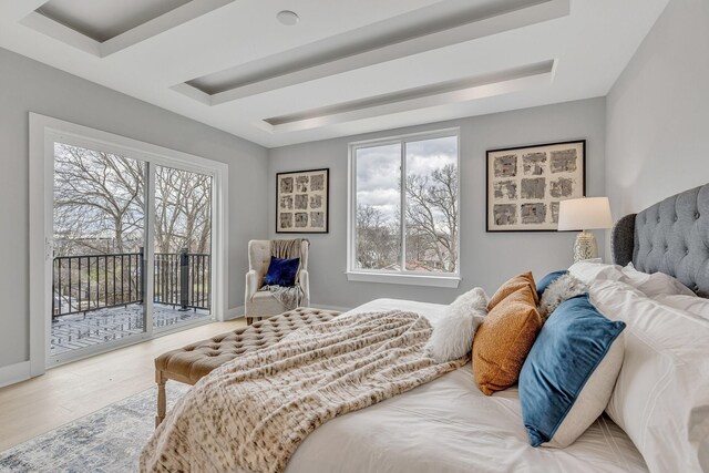 bedroom with a tray ceiling, access to outside, and hardwood / wood-style floors