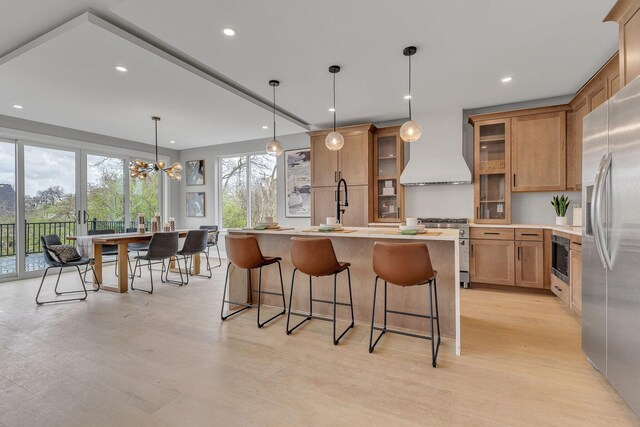 kitchen featuring an inviting chandelier, appliances with stainless steel finishes, a center island, custom exhaust hood, and light wood-type flooring