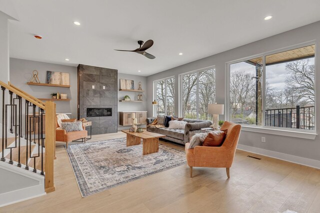 living room featuring ceiling fan, a tiled fireplace, and light hardwood / wood-style flooring