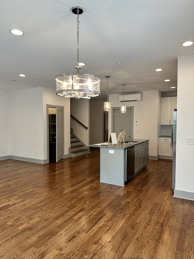 kitchen featuring hanging light fixtures, stainless steel appliances, dark hardwood / wood-style flooring, white cabinetry, and a kitchen island with sink