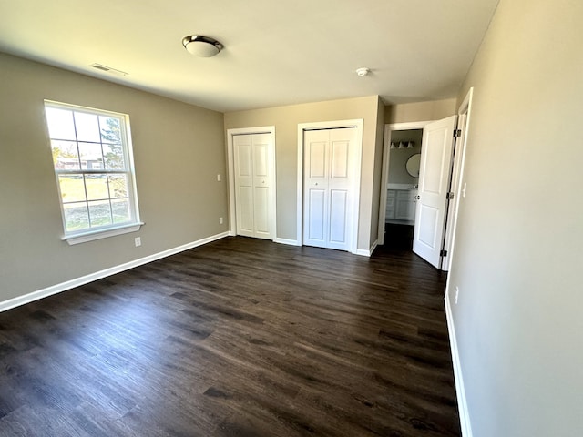 unfurnished bedroom featuring multiple closets and dark hardwood / wood-style floors