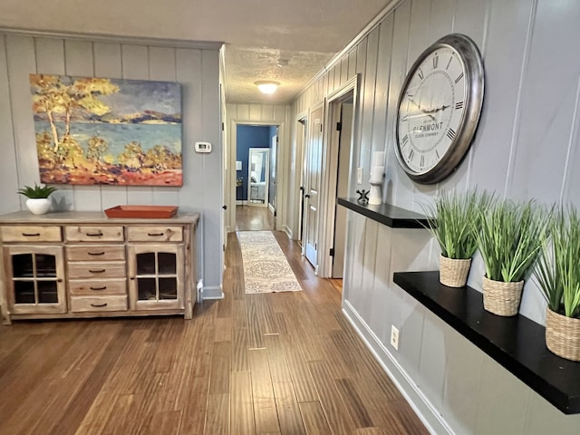 hallway with a textured ceiling, dark wood-type flooring, and wood walls